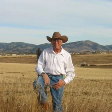 A man in cowboy hat standing on dry grass.